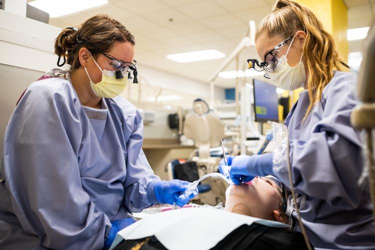 两名牙科卫生专业的学生在UMKC牙科诊所清洁一个人的牙齿
